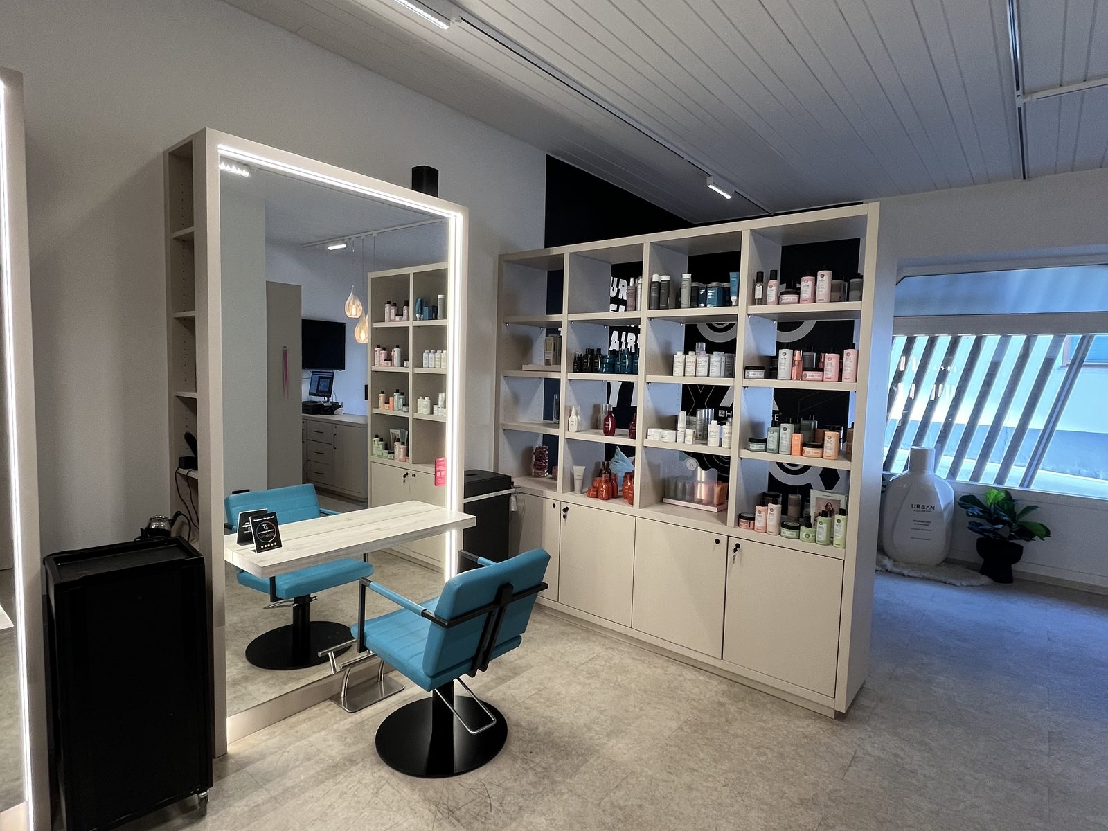 Einzelner Stylingplatz im HAIRLODGE Ellmau neben einem großen Regal mit Pflegeprodukten und Tageslicht vom Fenster.