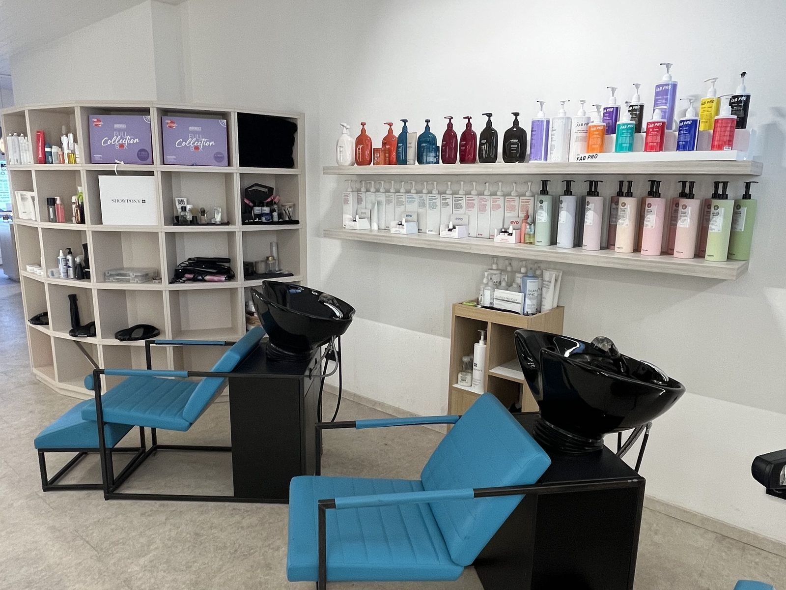Waschbereich im HAIRLODGE Ellmau mit petrolfarbenen Waschliegen und einem Regal voller Farb- und Pflegeprodukte.