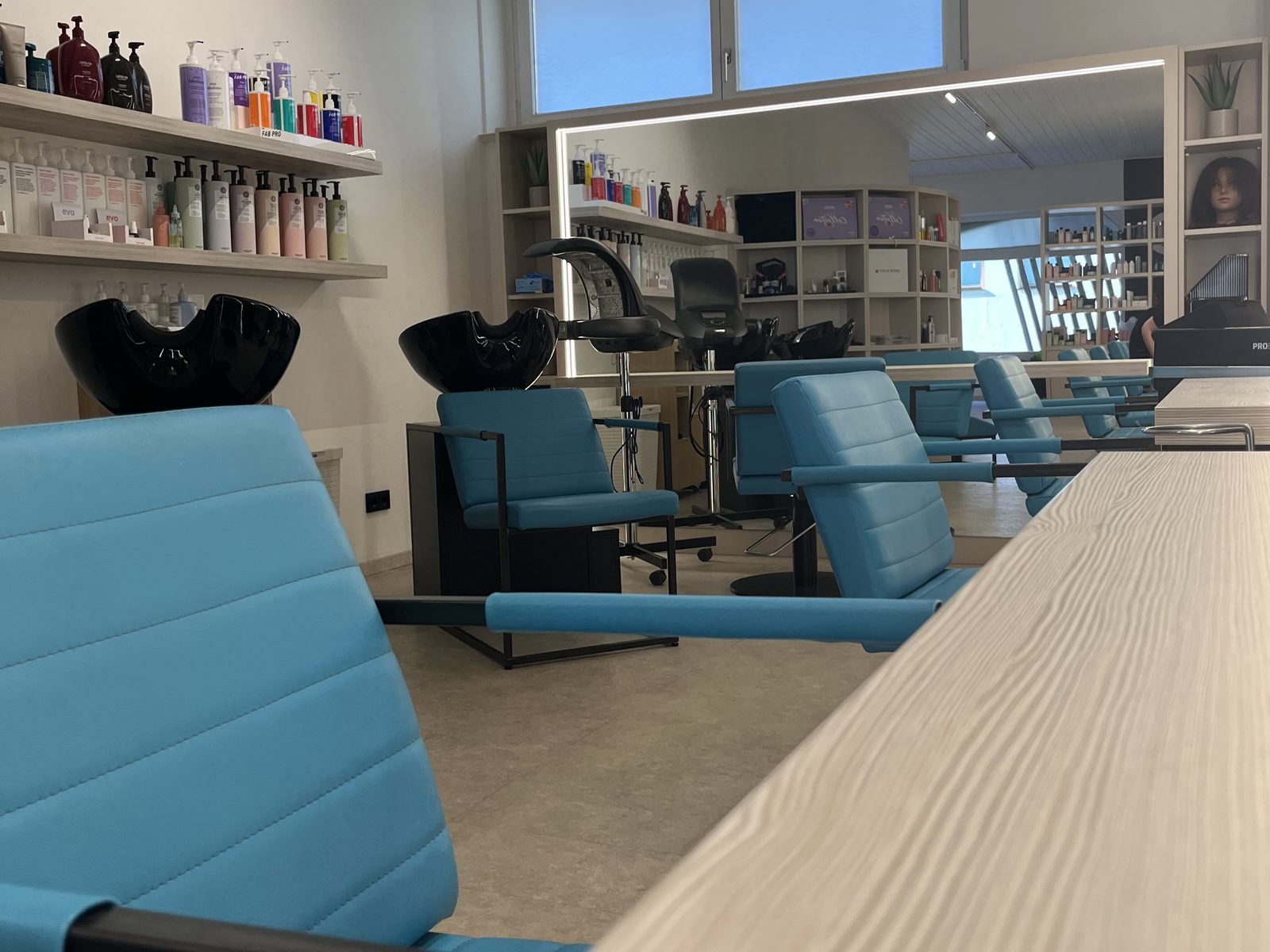 Stylingplaetze im HAIRLODGE Ellmau: petrolfarbene Sessel an der hellen Holzkonsole vor den beleuchteten Spiegeln.