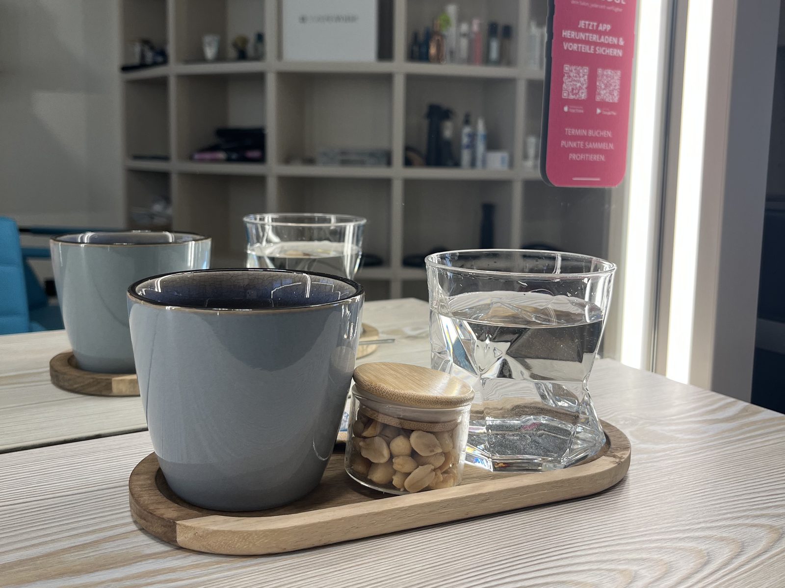 Kaffee und Wasser auf einem Holztablett im HAIRLODGE Ellmau, im Hintergrund der Hinweis auf die HAIRLODGE App.