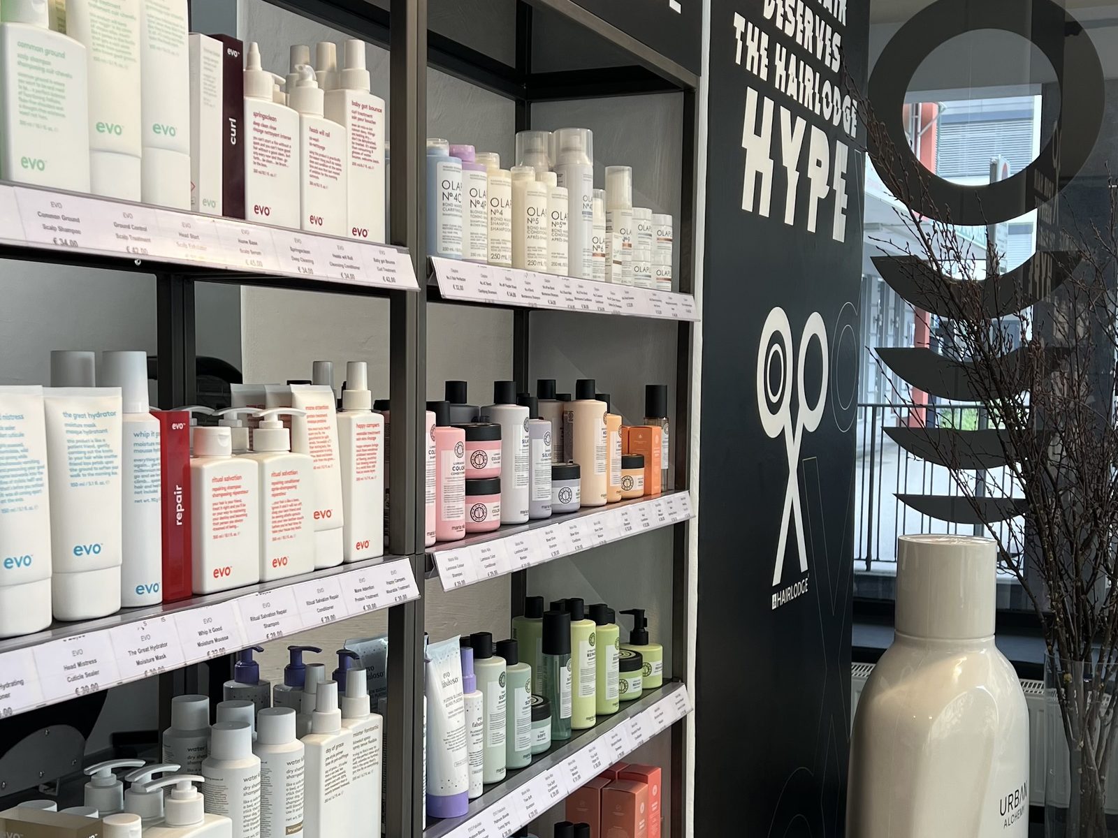 Produktwand im HAIRLODGE Kufstein mit evo, Olaplex, Maria Nila und Urban Alchemy neben dem Schriftzug "Your hair deserves the HAIRLODGE hype".