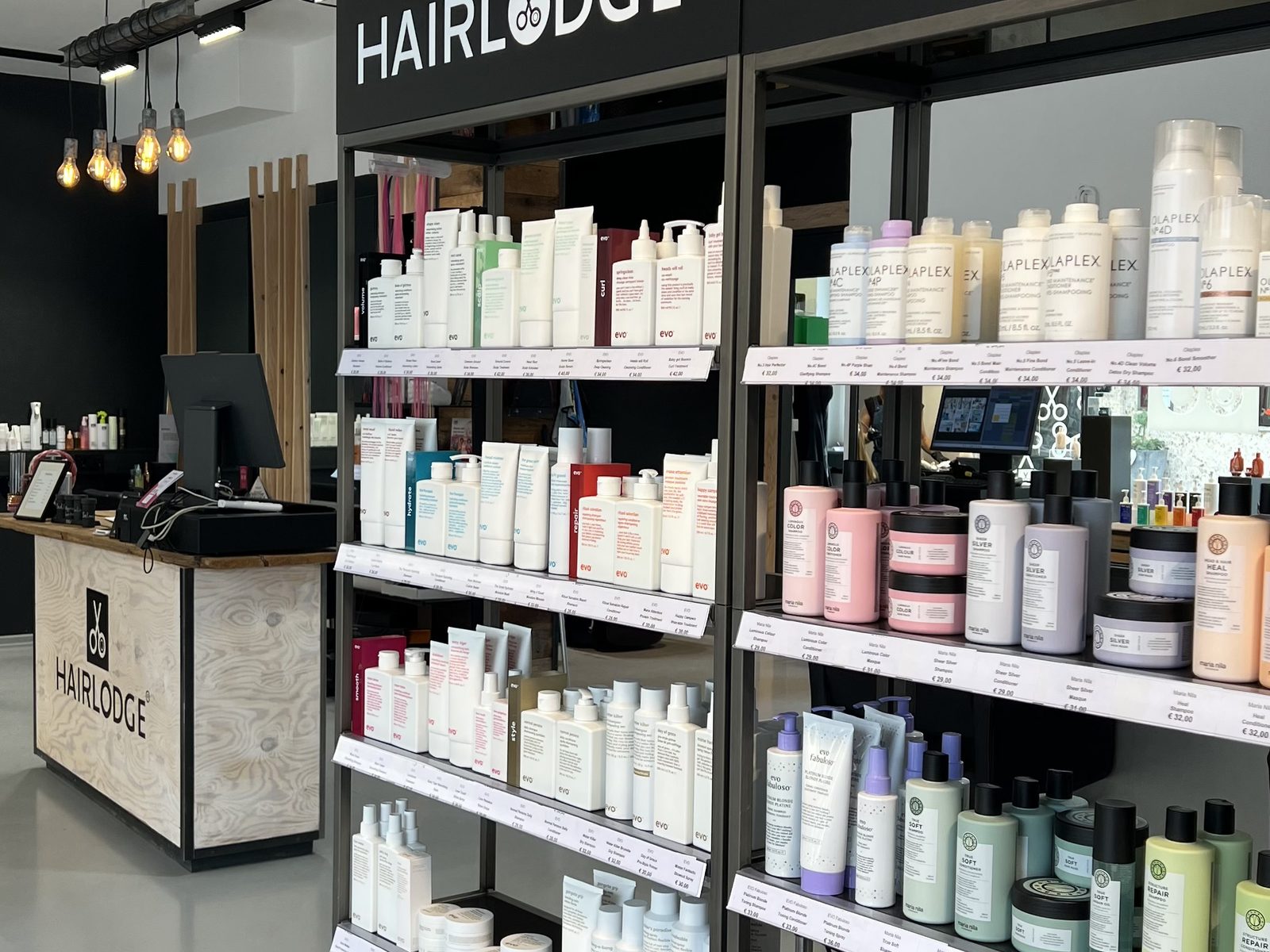 Verkaufsregale mit evo, Olaplex und Maria Nila unter den HAIRLODGE-Schildern, dahinter die Rezeption im HAIRLODGE Kufstein.