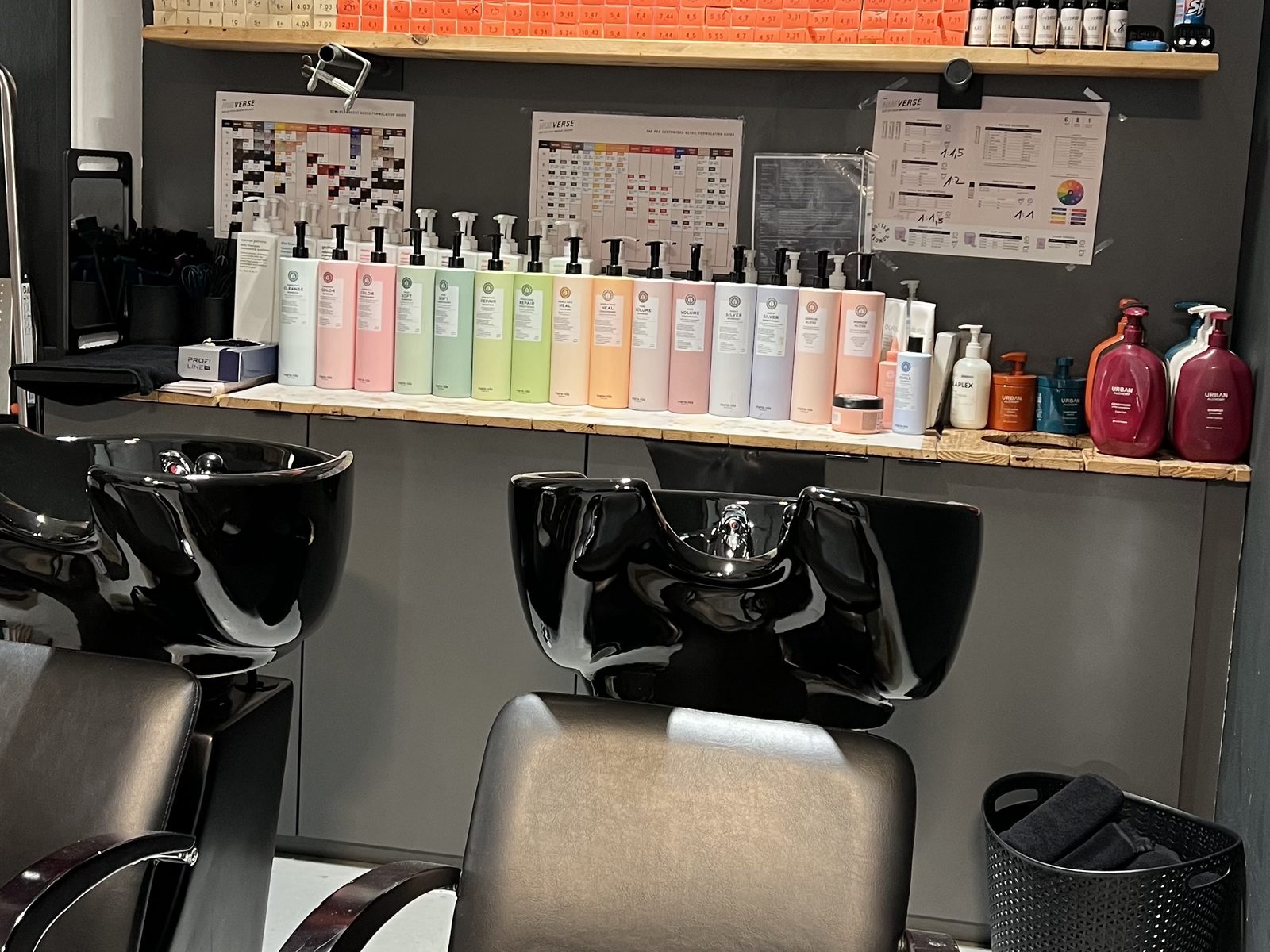 Waschbereich im HAIRLODGE Kufstein mit schwarzen Waschbecken vor der Holzregalwand mit Pflegeprodukten.