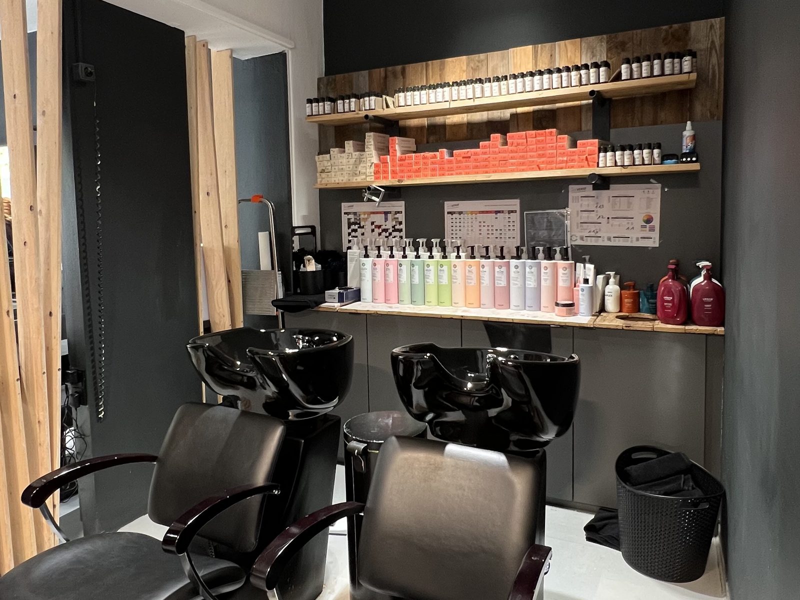 Waschraum im HAIRLODGE Kufstein mit zwei Waschplätzen, Farbregal und der Holzlattenwand am Übergang zum Salon.