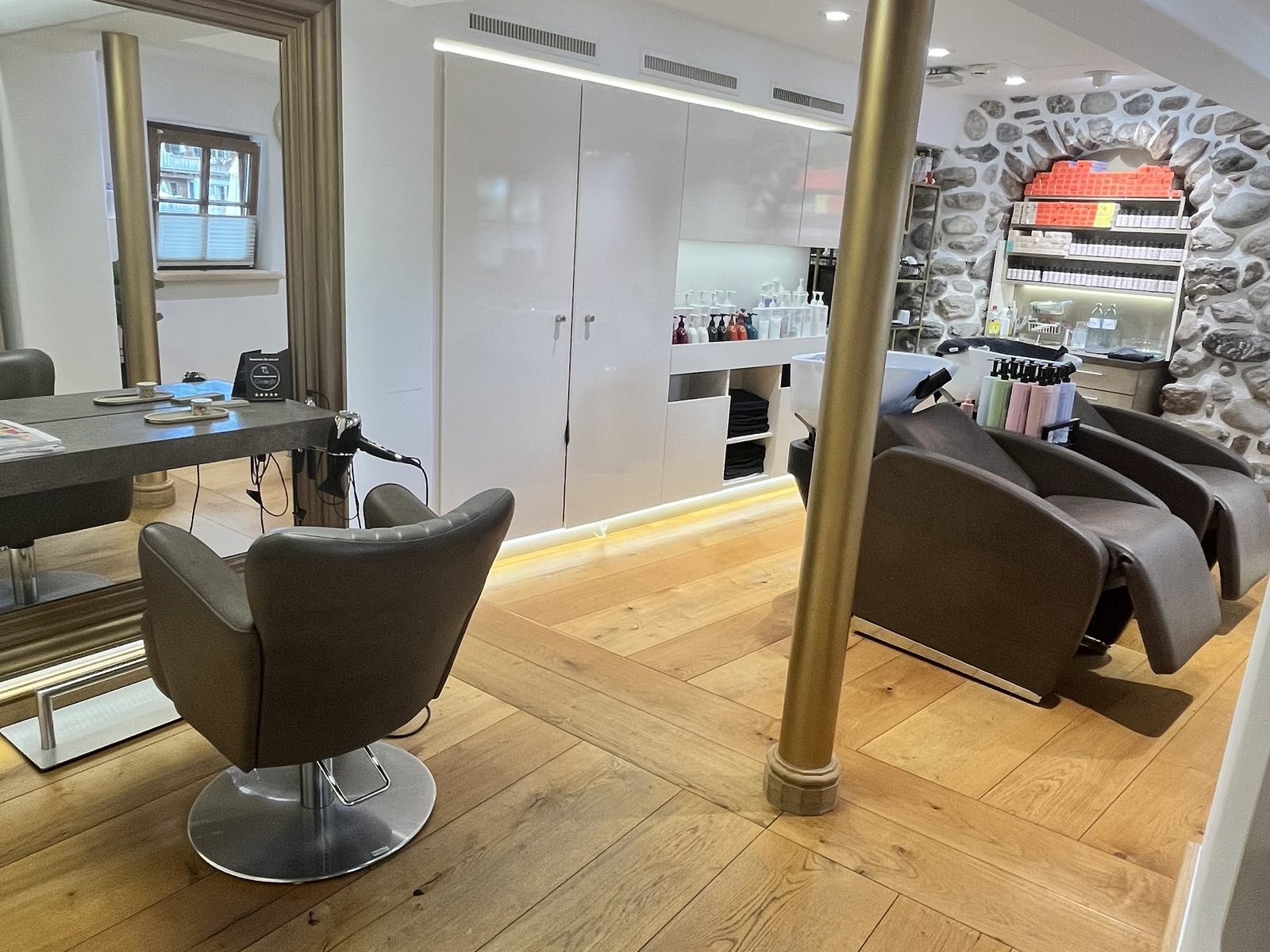 Blick in den HAIRLODGE Stanglwirt: Stylingplatz mit großem Spiegel, Messingsäule und dahinter der Waschbereich vor der Natursteinmauer.