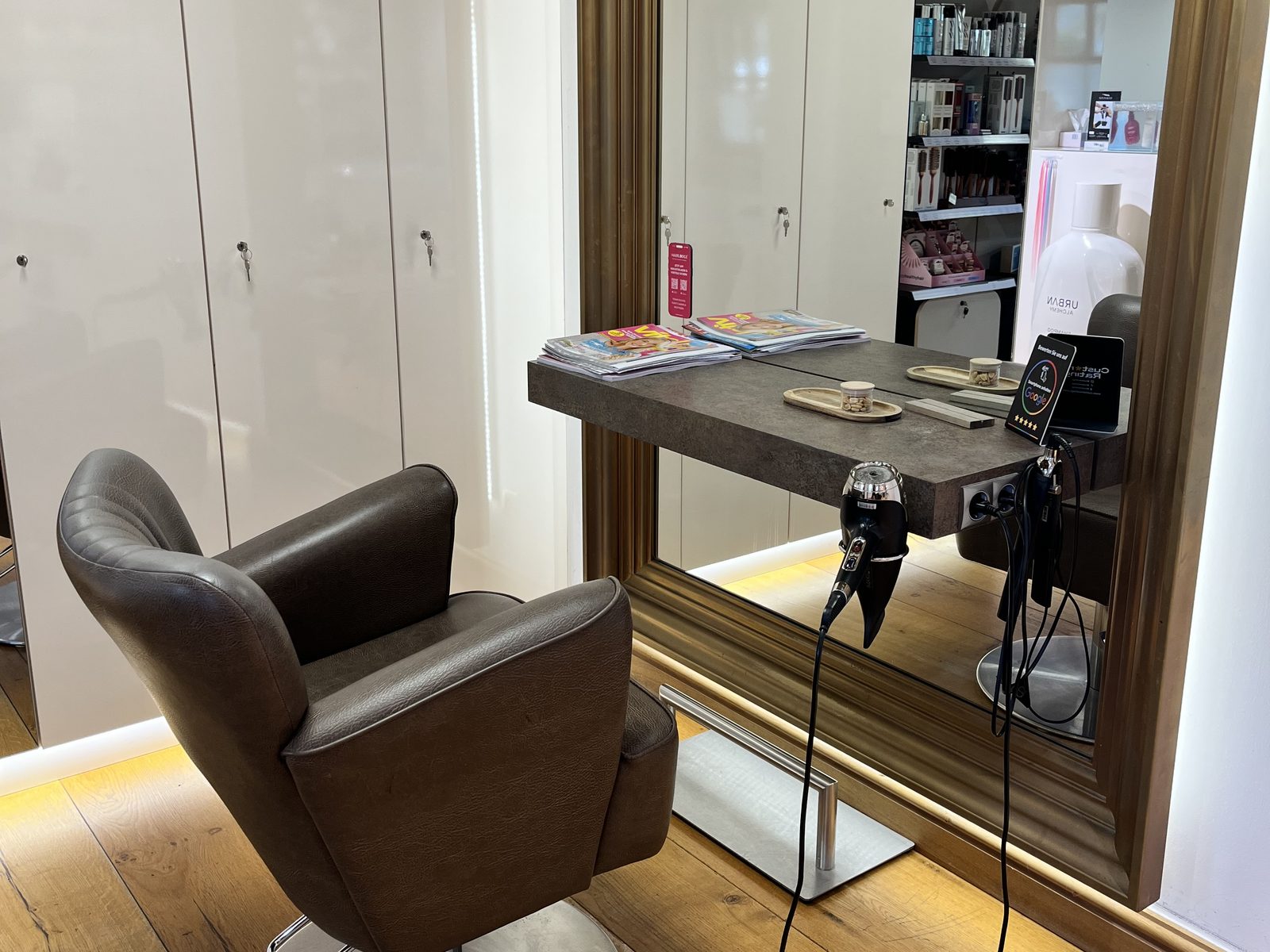 Stylingplatz im HAIRLODGE Stanglwirt mit goldgerahmtem Spiegel, braunem Ledersessel und Konsole auf Eichendielen.